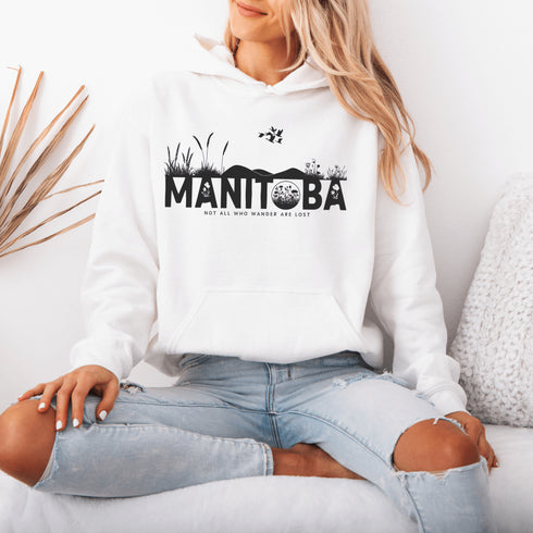 Featuring a prairie landscape, the design showcases wildflowers and prairie grasses blooming from the letters "Manitoba," artfully integrated into the scene.